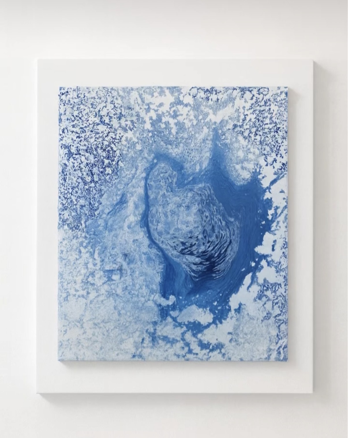 Abstract painting in layered cobalt and pale blue, with a deep swirling form at its centre surrounded by lace-like patterns, hung on a white wall
